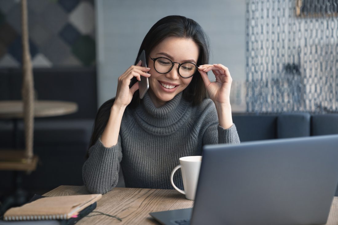 Cheerful Female Executive Have Conversation By Mobile Phone With Client At Coworking Place