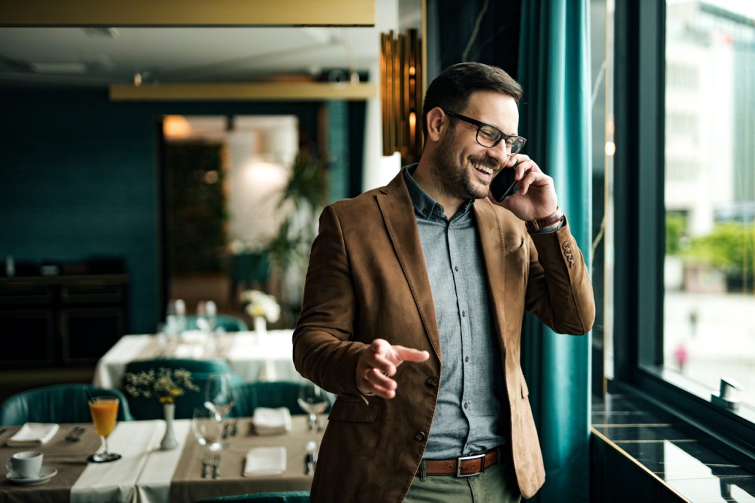 Portrait Of A Smiling Businessman In Restaurant Talking On Smart