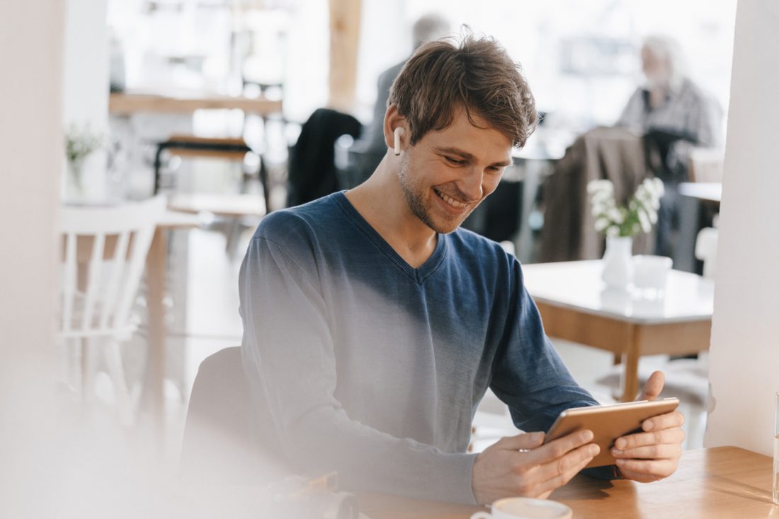 Smiling Man In A Cafe With Earphone Using Tablet