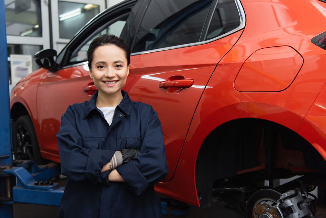 Young Workwoman Smiling At Camera Near Car In Garage